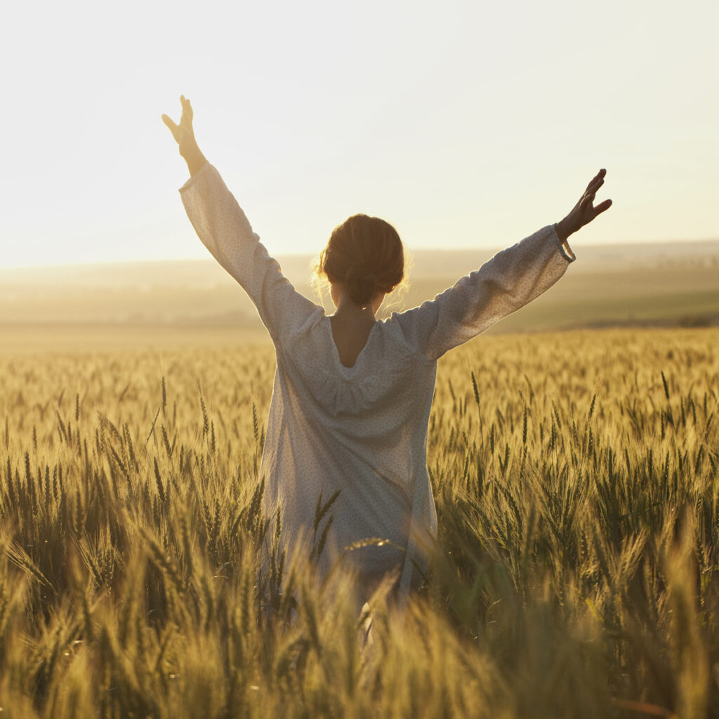 A person with arms raised in a sunlit field